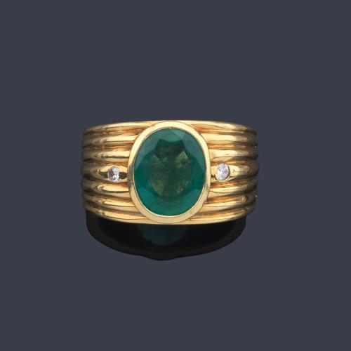 Anillo con esmeralda talla oval de aprox. 3,00 ct con dos brillantitos, en montura de oro amarillo de 18K con diseño gallonado.