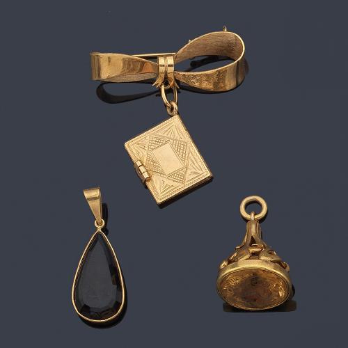Lote con dos colgantes con cuarzo ahumado talla perilla y cuarzo citrino tipo 'intanglio', con motivo de lazada y pequeño librito con inscripciones, en montura de oro amarillo de 18K.