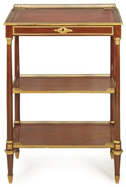 Mesa de escritorio alta Luis XVI en madera de caoba, con tapa superior de cuero marrón gofrado y dorado, sobre montantes en forma de columna con estantes intermedios. Aplicaciones de latón. 