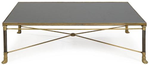 Mesa de centro baja con tapa de cristal negro sobre patas en forma de columnas acabadas en garras de animal en bronce.