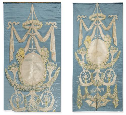  Dos paños muralesde seda Luis XVI, la composición se articula en torno a una reserva central oval, enmarcada por guirnaldas florales, cintas ondulantes, roleos y caídas de follaje sobre fondo liso azul. 