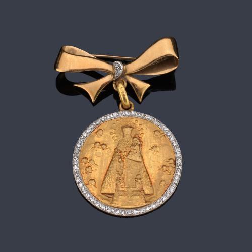 Broche con medalla devocional con La Virgen de los desamparados enmarcado con brillantes y motivo superior en forma de lazada.