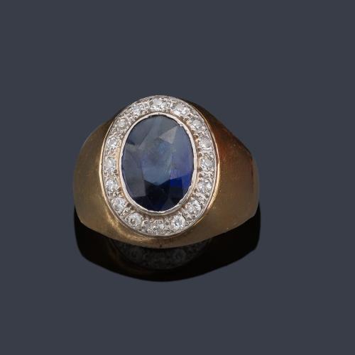  Anillo tipo sello con zafiro talla oval y orla de brillantes, en montura de oro amarillo de 18K.