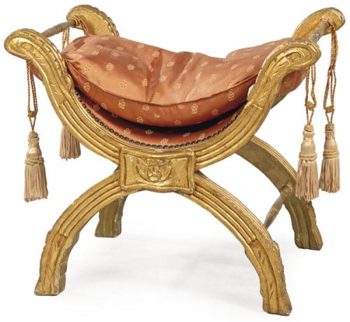Taburete estilo Savonarola con estructura de madera tallada y dorada y cojín de seda rosa con borlas.