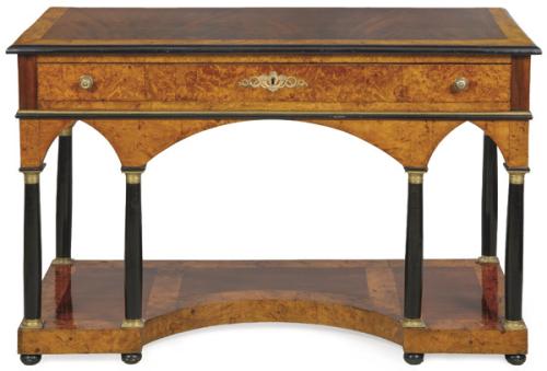  Consola Fernandina de diseño arquitectónico en madera de raíz, articulada sobre un frente recto con cajón central largo y dos cortos, sobre montantes en forma de columnas toscanas ebonizadas, con basas y capiteles en bronce que sostienen arcos ojivales. S