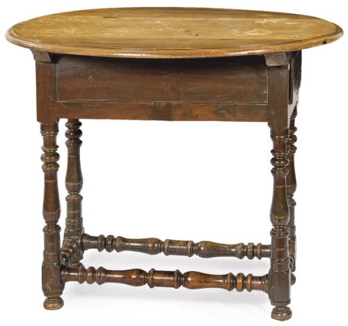  Mesa de tapa ovalada en madera de nogal, sobre patas unidas por chambranas torneadas.