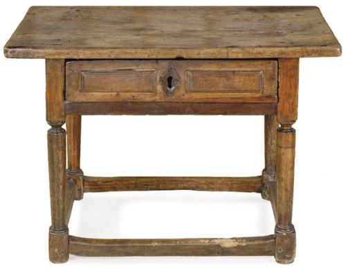Mesa bufete, con tapa rectangular en madera de nogal, con un cajón en el frente, con cuarterones y escudo de cerradura en hierro, sobre montantes en forma de columnas toscanas unidas por chambranas rectas en la parte inferior. España, S. XVII