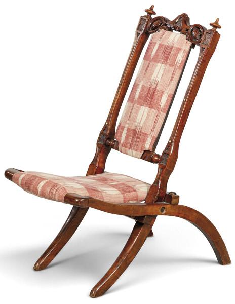  Silla plegable sin brazos, en madera tallada, calada y torneada, con respaldo alto inclinado y base articulada de tijera.