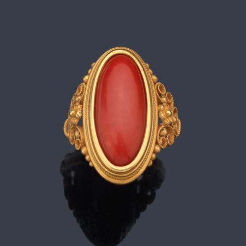  Anillo lanzadera con pieza de coral talla cabujón en montura decorada con cordoncillo y volutas en oro amarillo de 18K.