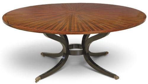  Mesa de comedor de tapa circular en madera chapada, con composición radial mediante chapas de madera de palisandro y canto perimetral. Se apoya sobre estructura central de elementos curvos de madera con acabado negro unidos en el centro por elemento en